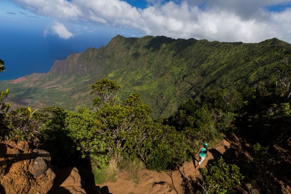 Hiker on a red-dirt trail in Kōkeʻe above Kalalau Valley
