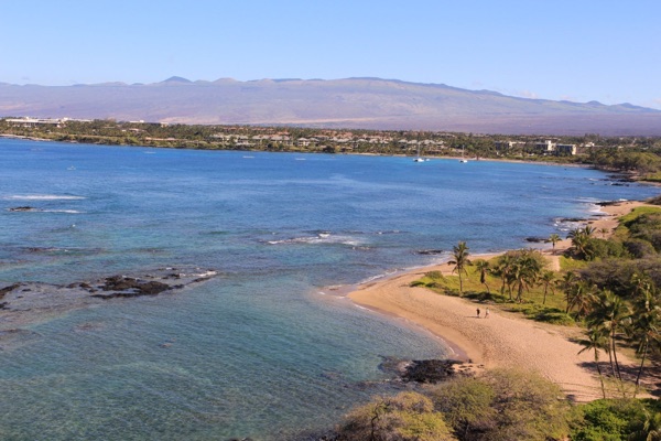 Kona Coast shoreline and resort bay with Hualālai and Mauna Kea behind
