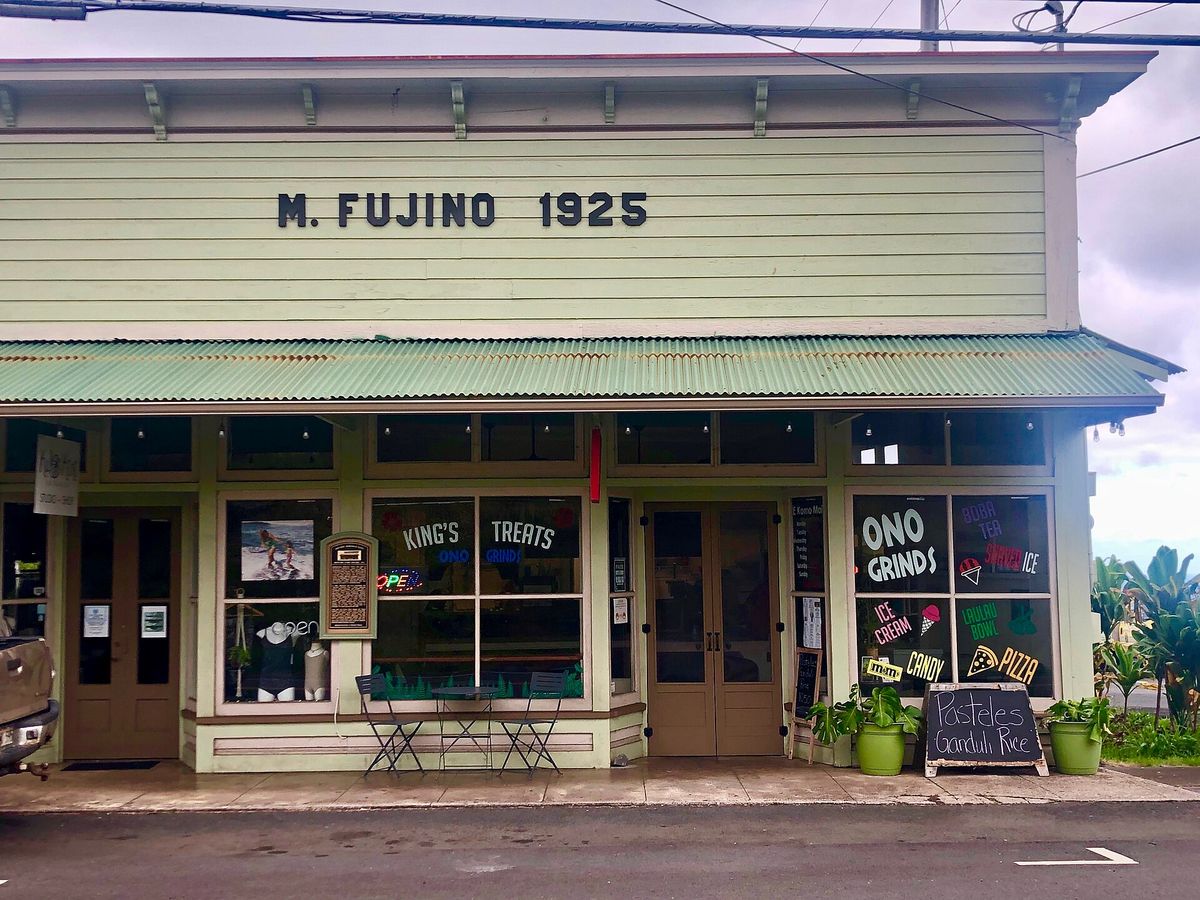 The pale green wooden M. Fujino 1925 building with a metal awning, shop windows and café signs.