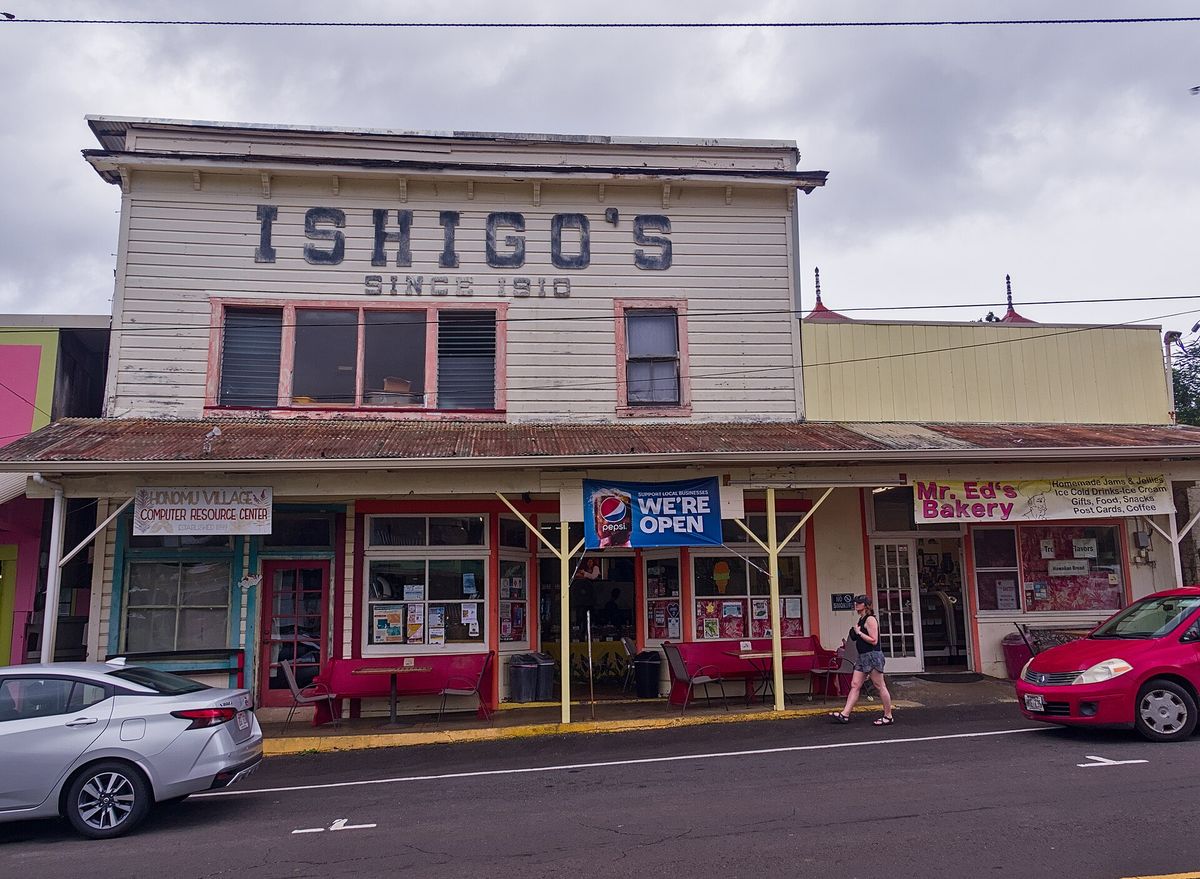 The two-story wooden Ishigo’s General Store building on Honomū’s main street, with shop fronts and parked cars.