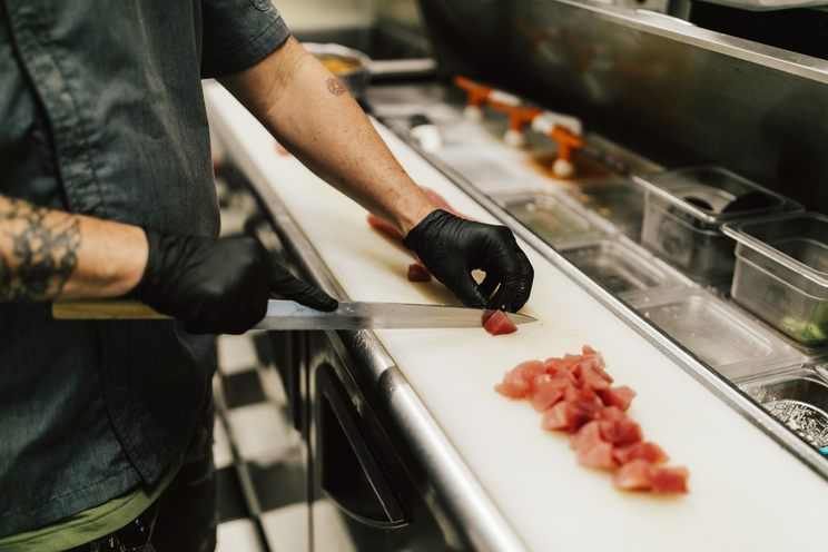A chef in gloves cutting fresh raw fish into cubes for poke