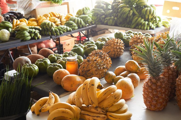 Market table piled with bananas, pineapples, papayas, and other tropical fruit