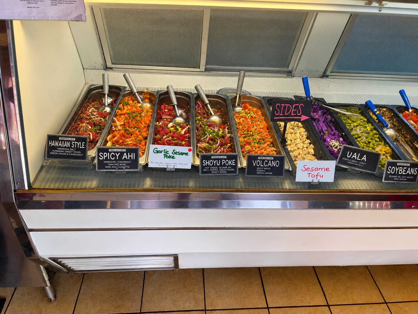 Glass deli case filled with trays of colorful poke and prepared foods