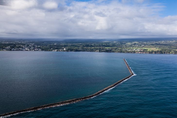 Aerial view of the long rock breakwater stretching across Hilo Bay under a cloudy sky