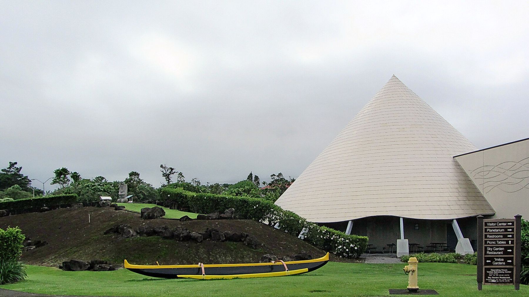The white cone-shaped roofs of ʻImiloa Astronomy Center beyond a lawn and a native garden