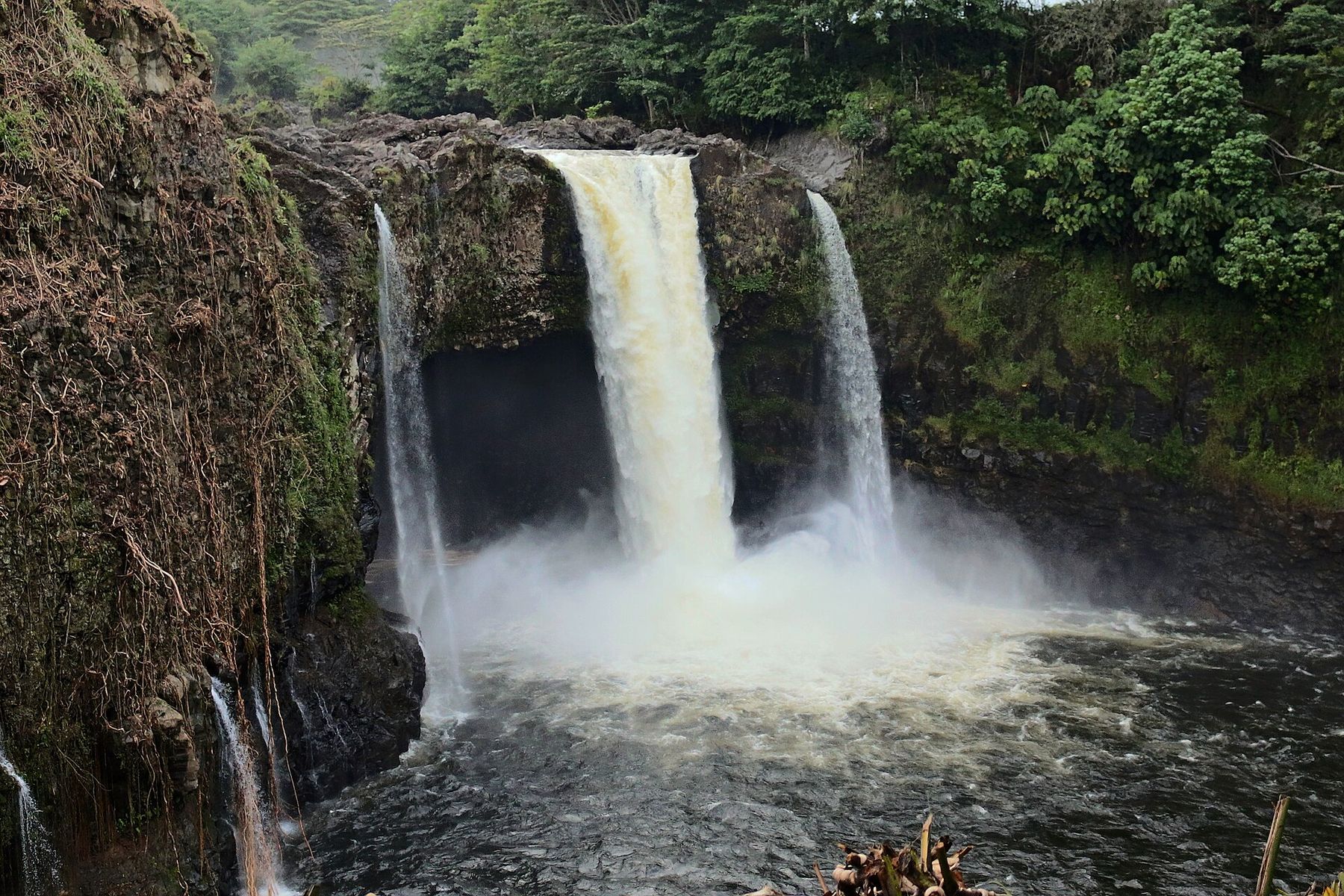Waiānuenue (Rainbow Falls) pouring over a lava ledge into a misty pool framed by green rainforest