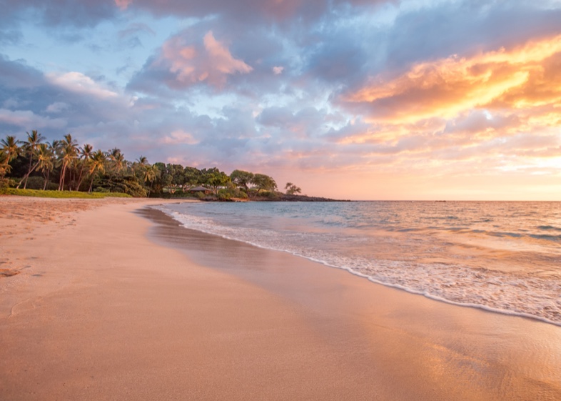 Kaunaʻoa Beach at sunset, with orange and pink clouds reflected in the wet sand and palms on the left