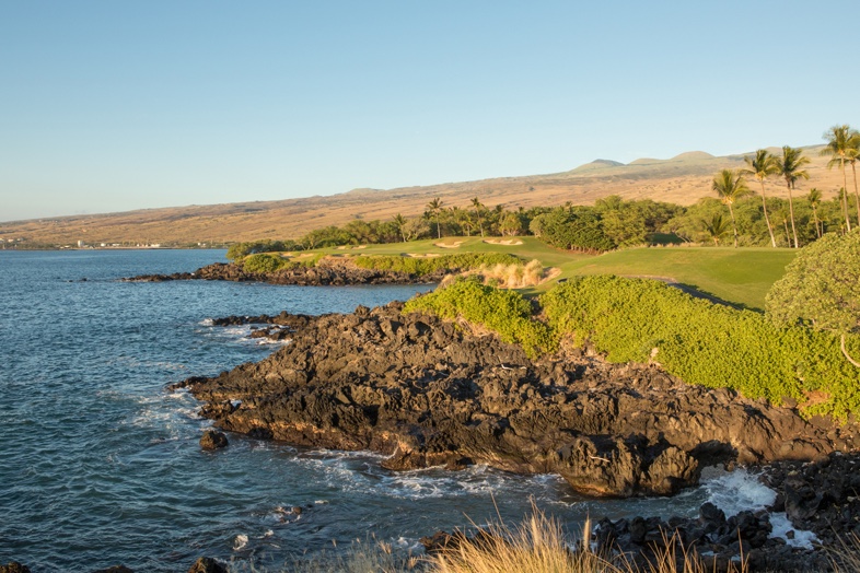 A green golf fairway beside a rocky shoreline and deep blue sea on the Kohala Coast