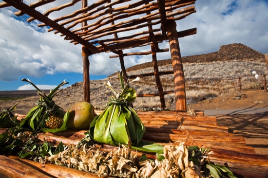 Hoʻokupu offerings wrapped in green ti leaves resting on a wooden platform at a heiau