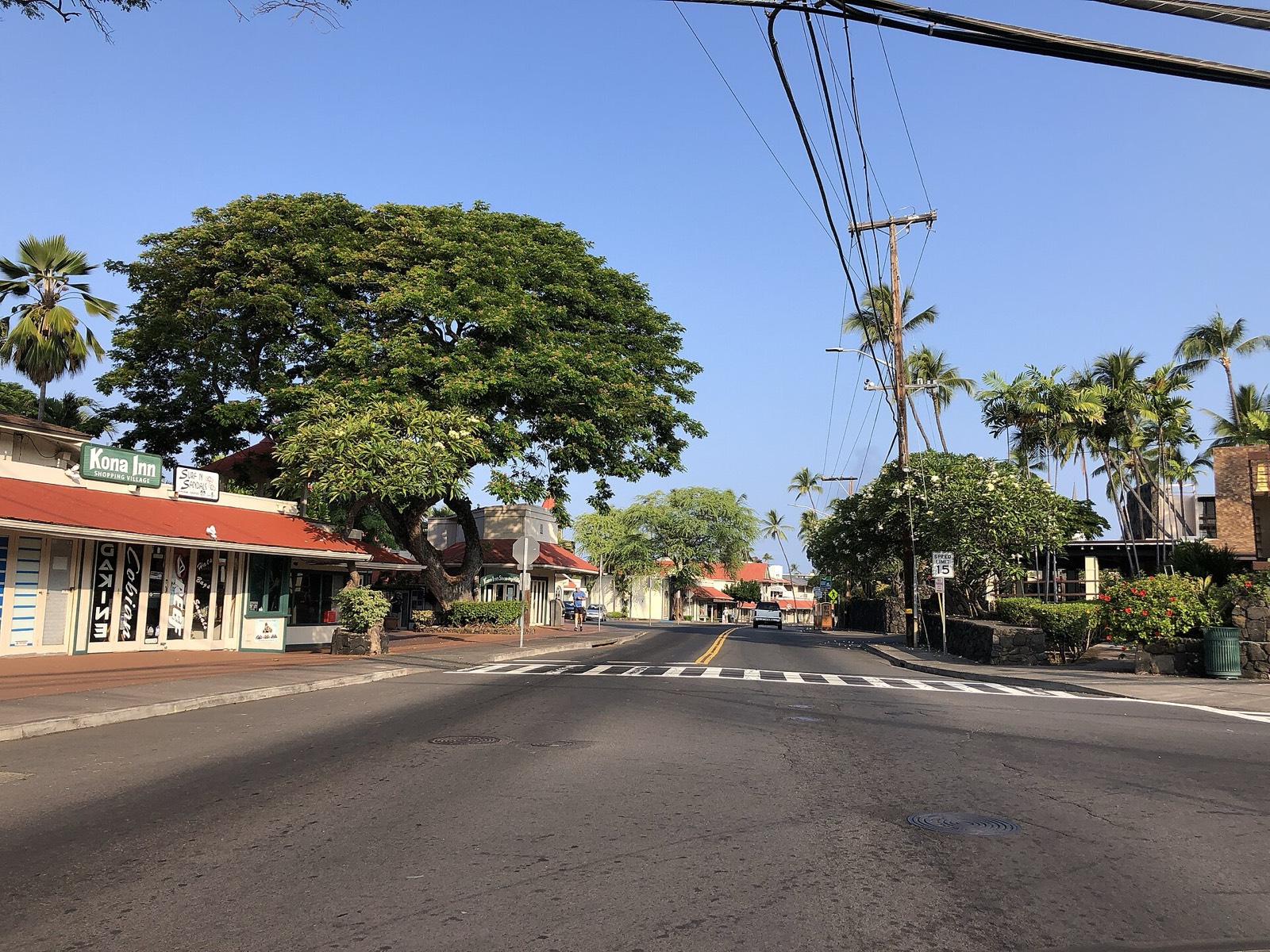 Aliʻi Drive at Hualālai Road in Kailua-Kona, with the Kona Inn Shopping Village under a large monkeypod tree