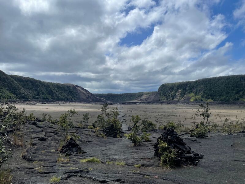 Hikers and stone cairns on the old lava-lake floor of Kīlauea Iki crater beneath its forested walls
