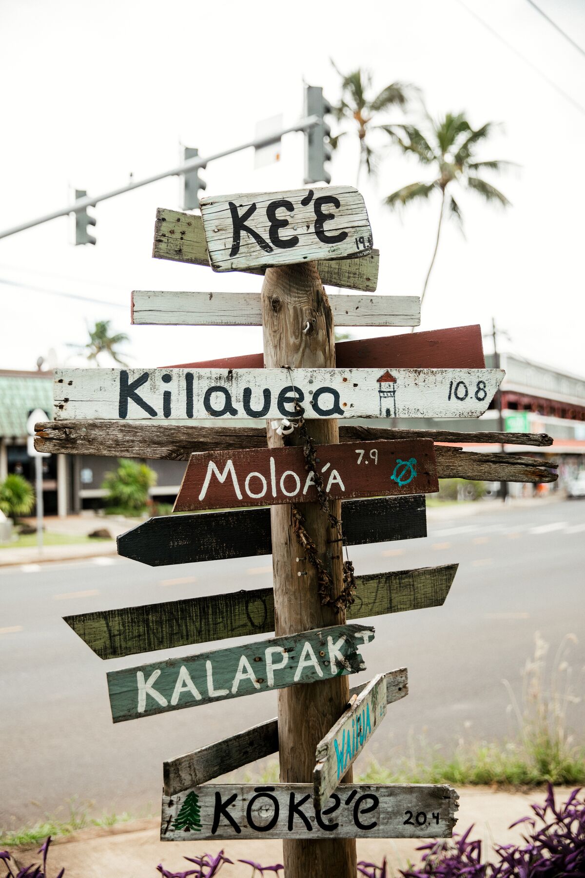 A weathered wooden signpost with hand-painted arrows for Keʻe, Kīlauea, Moloʻa, Kalapaki and Kōkeʻe