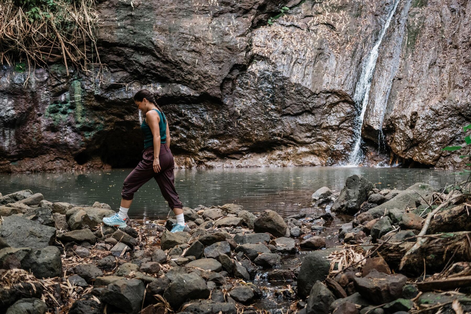 A woman beside a small waterfall at the foot of a rocky green cliff
