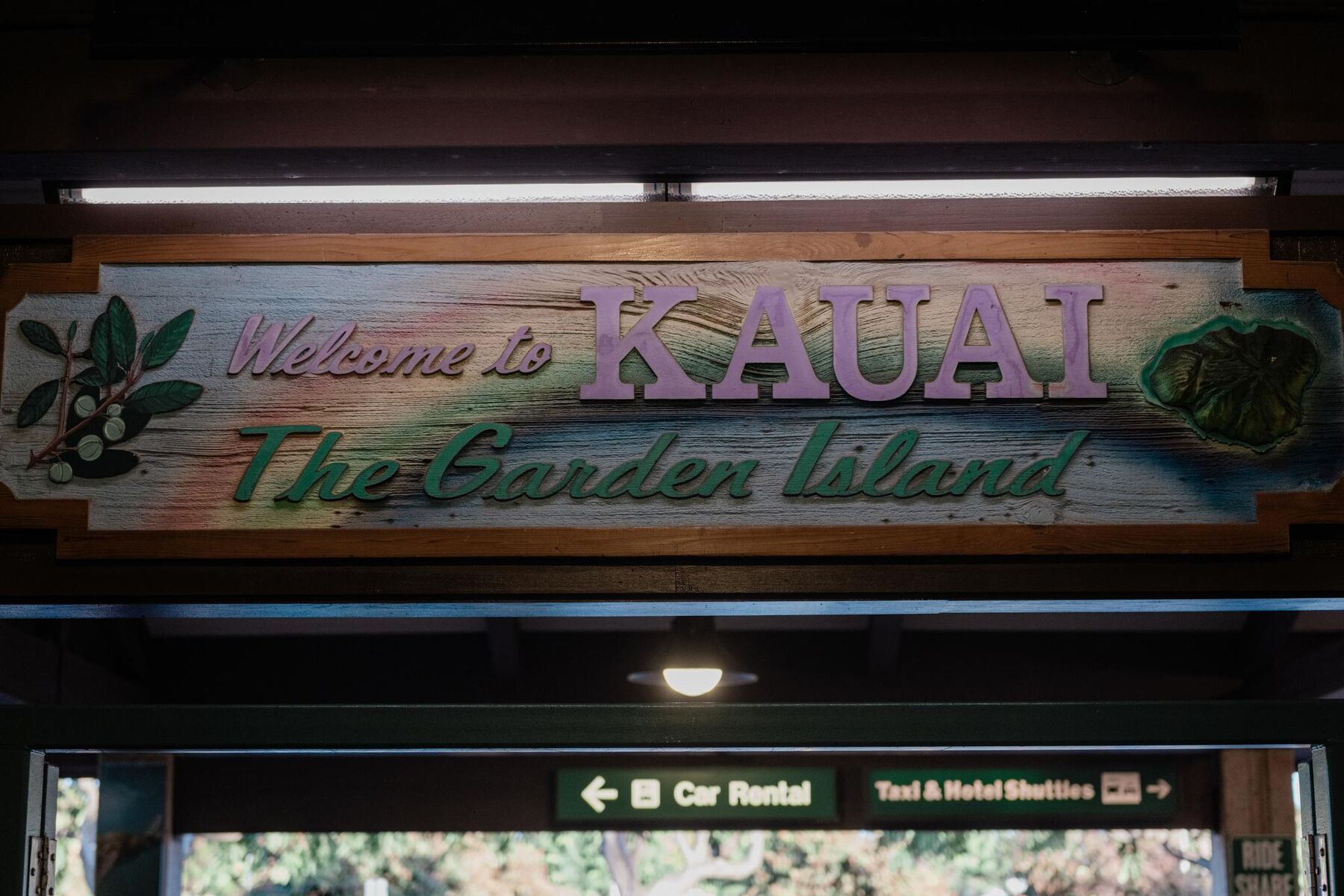A “Welcome to Kauaʻi – The Garden Island” sign at the airport, with directional signs below pointing to car rental and to taxis and hotel shuttles