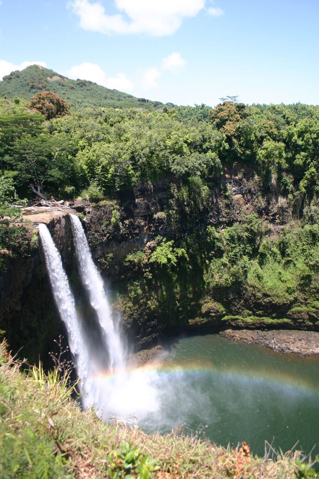 Wailua Falls from a different angle in bright sun, white water against dark rock and a turquoise pool