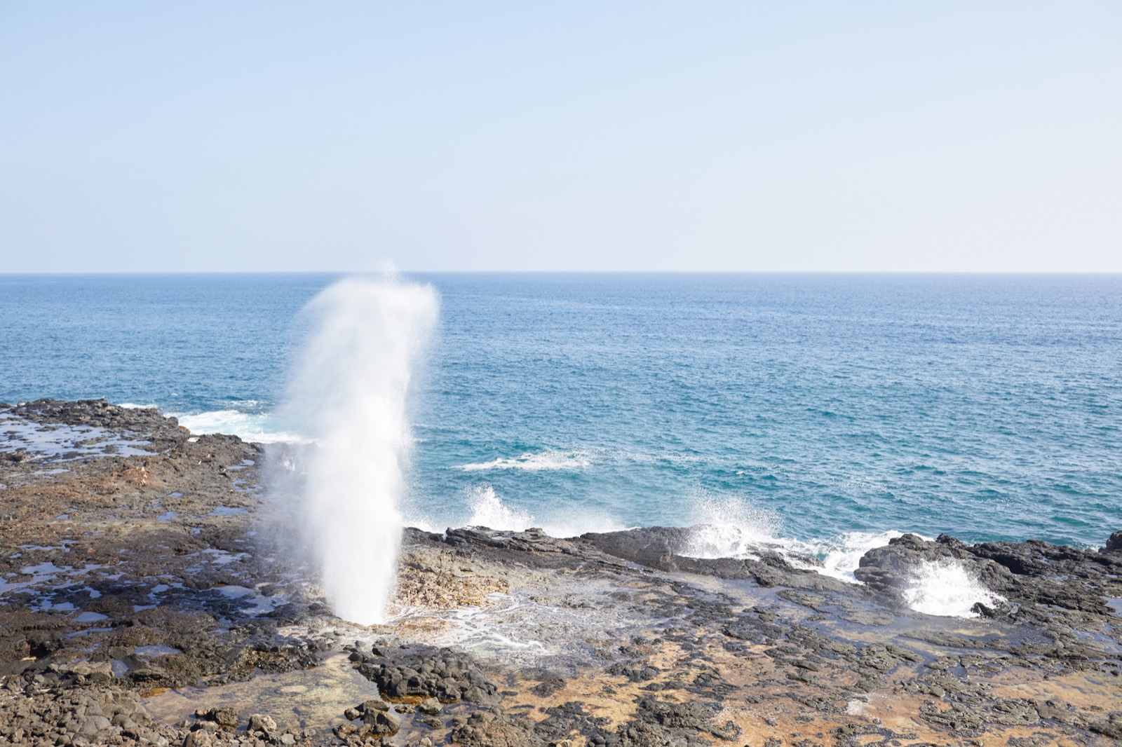 Spouting Horn blowhole shooting a tall plume of spray from the lava shelf beside the ocean