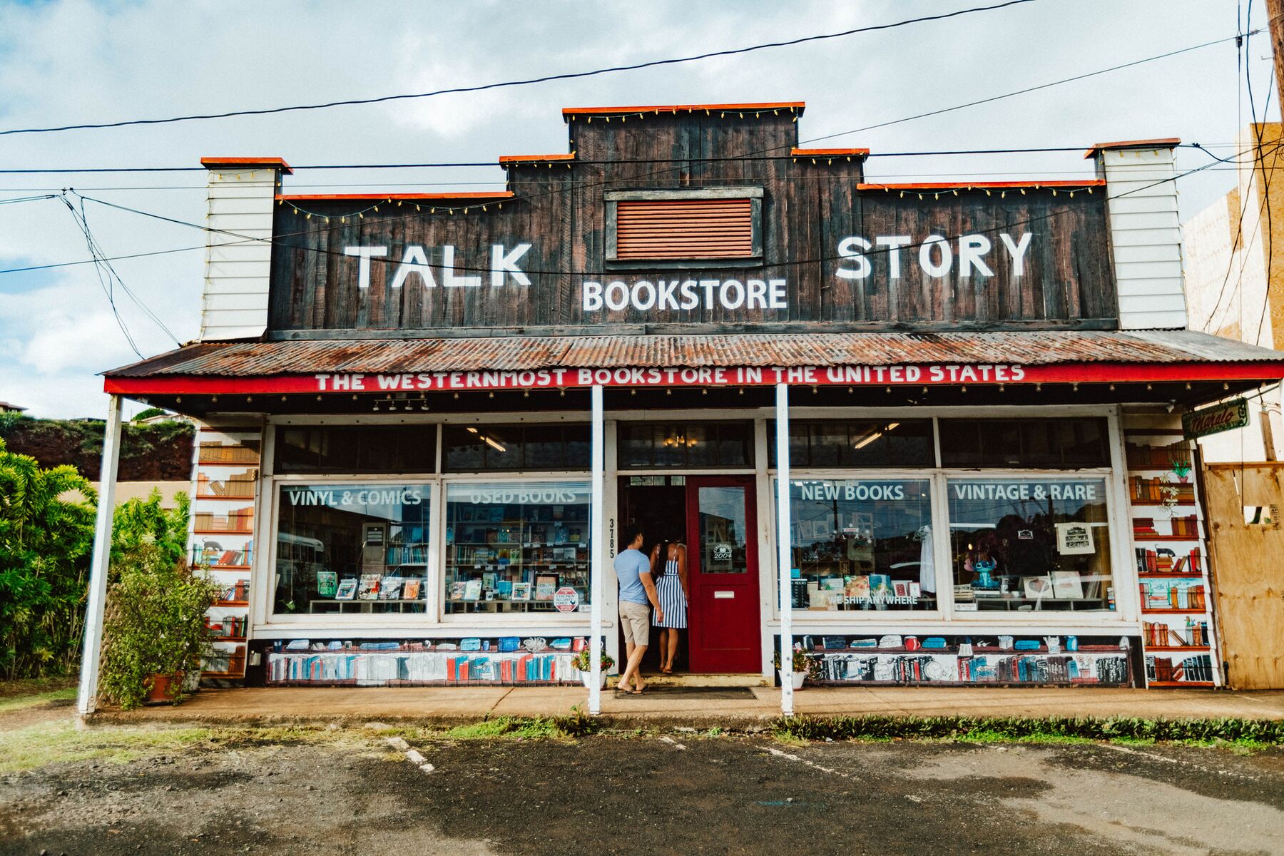 The wooden false-front Talk Story Bookstore in Hanapēpē, with a red banner reading “The westernmost bookstore in the United States” below the roofline, and two people walking in the open door