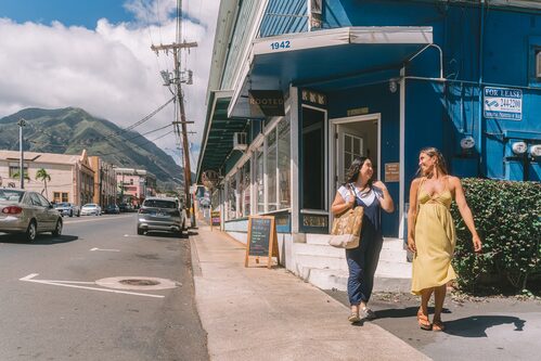 People walking past storefronts in Wailuku town, with the West Maui Mountains behind