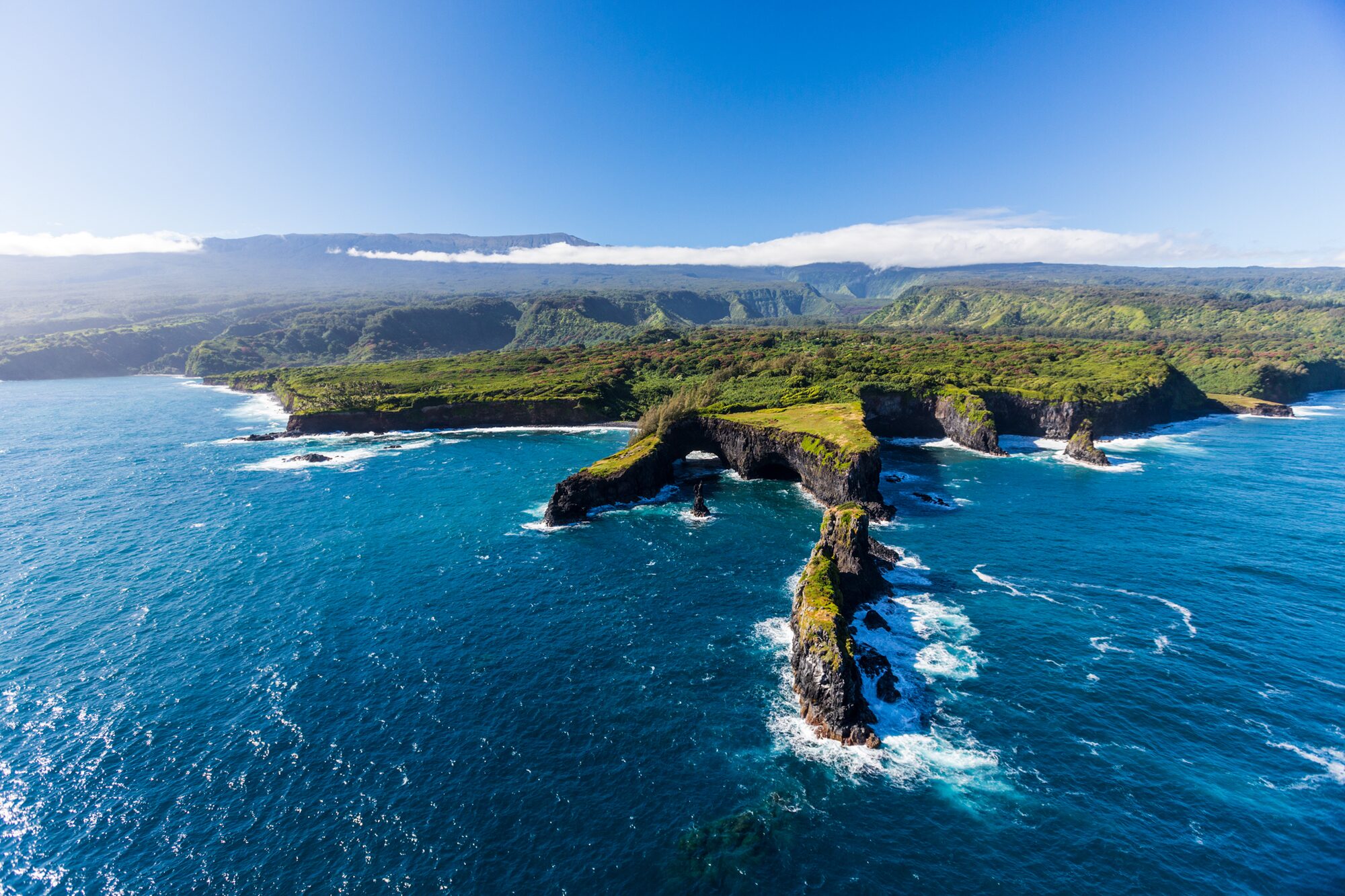 Aerial view of dark lava sea cliffs and a sea arch above turquoise water on the East Maui coast