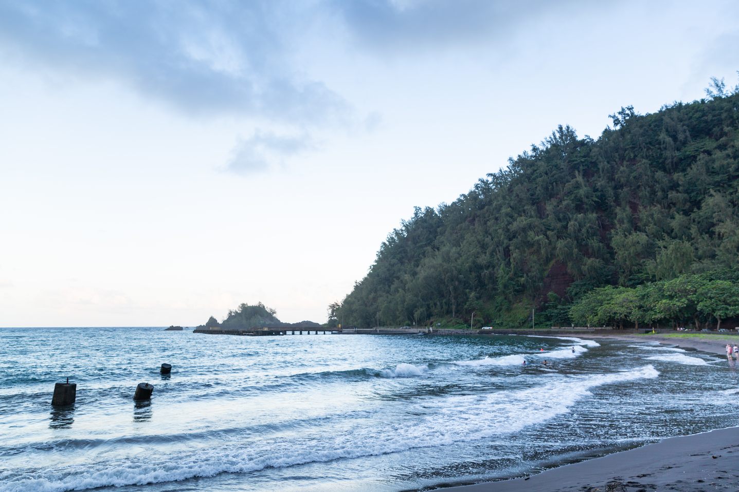 Hāna Bay with dark sand and steep forested hills