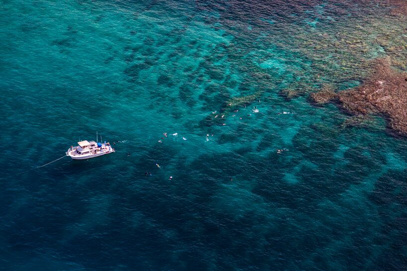 A snorkel boat above a clear turquoise reef off Mākena, seen from the air
