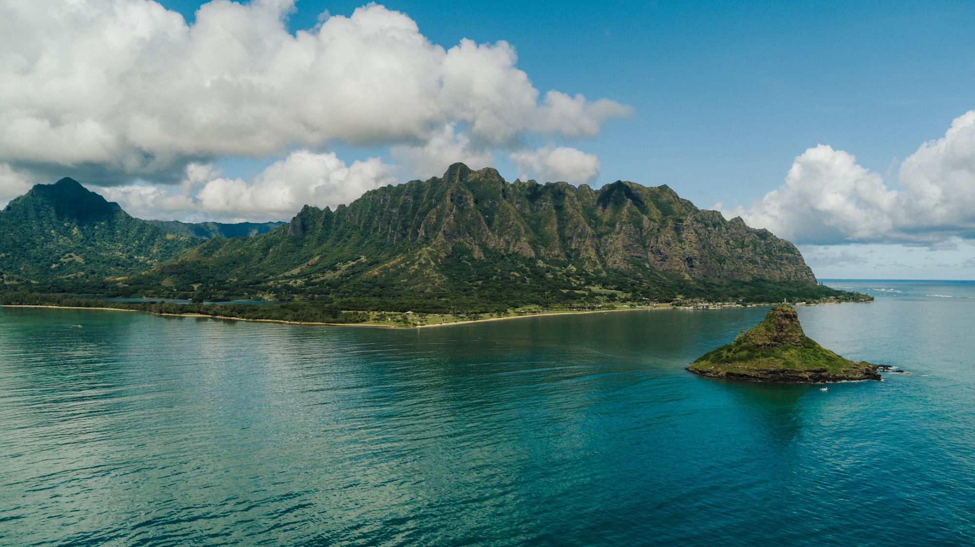 Mokoliʻi island rising from turquoise Kāneʻohe Bay below the jagged green Kualoa ridges